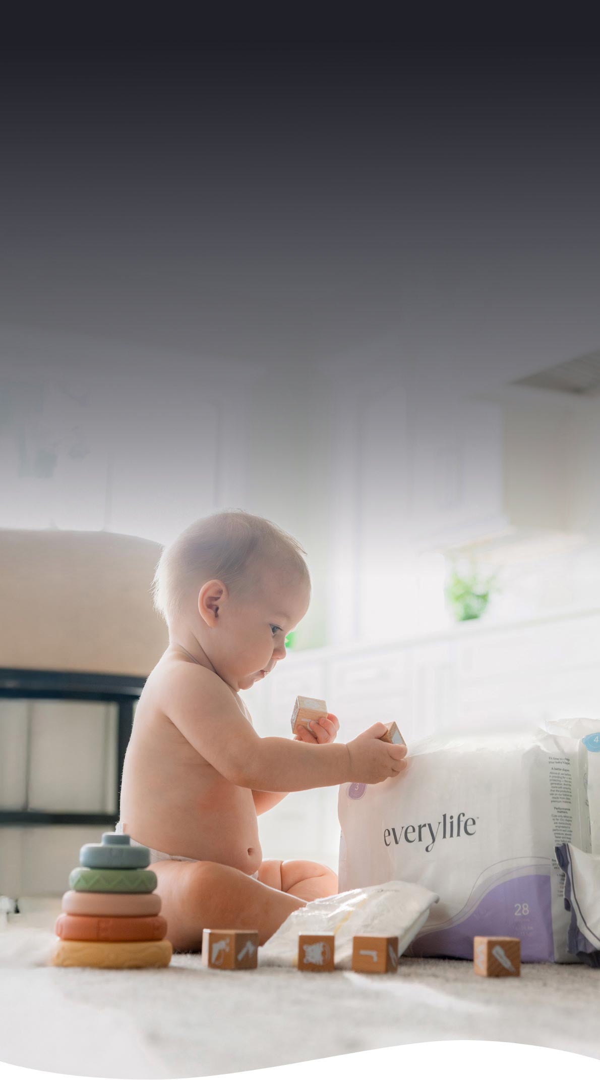 A baby sitting on a floor in a bright room, playing with blocks next to a pack of EveryLife baby wipes and diapers.